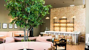 Een restaurant met ronde tafels, comfortabele zittingen, hanglampen, een bar in het midden en een grote binnenboom.