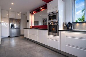 A modern kitchen with stainless steel appliances, white cabinetry, and a red accent wall. - Villa tropicale standing, Piscine&spa, Sainte anne (Sainte-Anne)