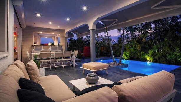 Uma área externa com piscina, bar e espaço de estar com sofá e cadeiras.