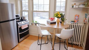 Une cuisine équipée d’un réfrigérateur, d’une cuisinière et d’un four, une table à manger avec des chaises, et une fenêtre donnant sur l’extérieur.