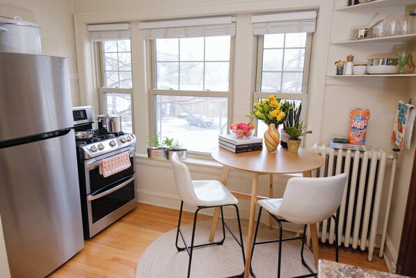 A kitchen with a refrigerator, stove, and oven, a dining table with chairs, and a window with a view of the outside.