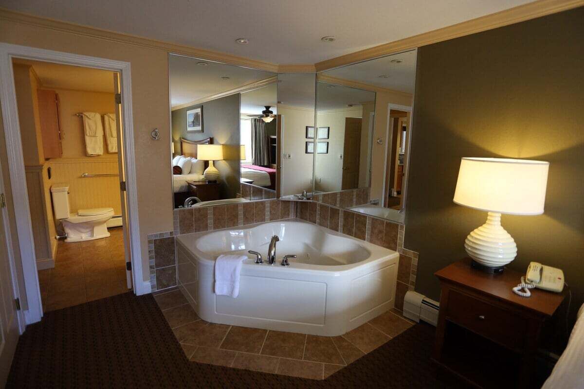 Un bagno moderno con una vasca da bagno grande, uno specchio, un comodino con una lampada e un WC visibile nella stanza adiacente.