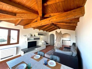 A modern living room with a fireplace, sofa, dining table, and kitchen area.