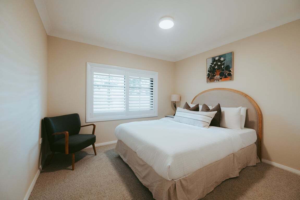 Quarto com uma cama, uma cadeira, uma janela com cortinas e um quadro na parede.