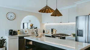 Une cuisine moderne dotée d’un grand îlot central, de luminaires suspendus, d’une horloge et d’un réfrigérateur.
