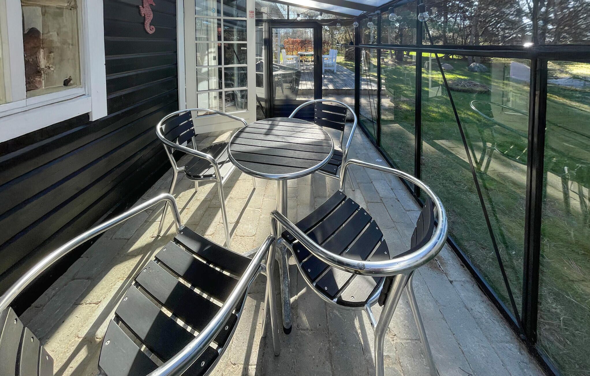 Un balcón con mesa y sillas, un ventanal de vidrio y vista a un patio.