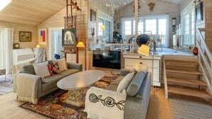Ein gemütliches Blockhauss-Interieur mit einer Couch, einem Fernseher, einer Essecke und einer Treppe.