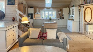 Ein gemütliches Blockhaushaus-Interieur mit einer Couch, einem runden Tisch, Holzböden, einer Küche mit Herd und einer Treppe.