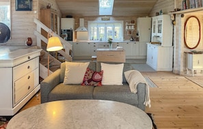 Ein gemütliches Blockhaushaus-Interieur mit einer Couch, einem runden Tisch, Holzböden, einer Küche mit Herd und einer Treppe.