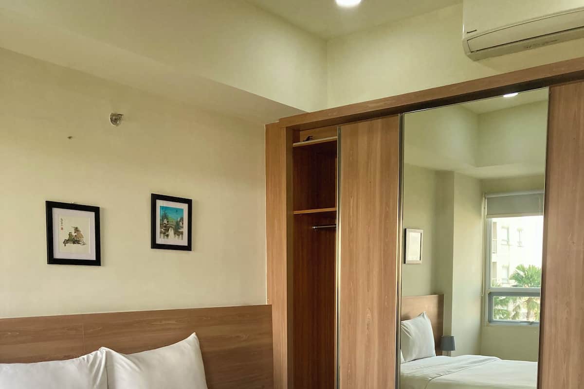 Habitación de hotel con una cama grande, un armario, un espejo y dos cuadros en la pared.