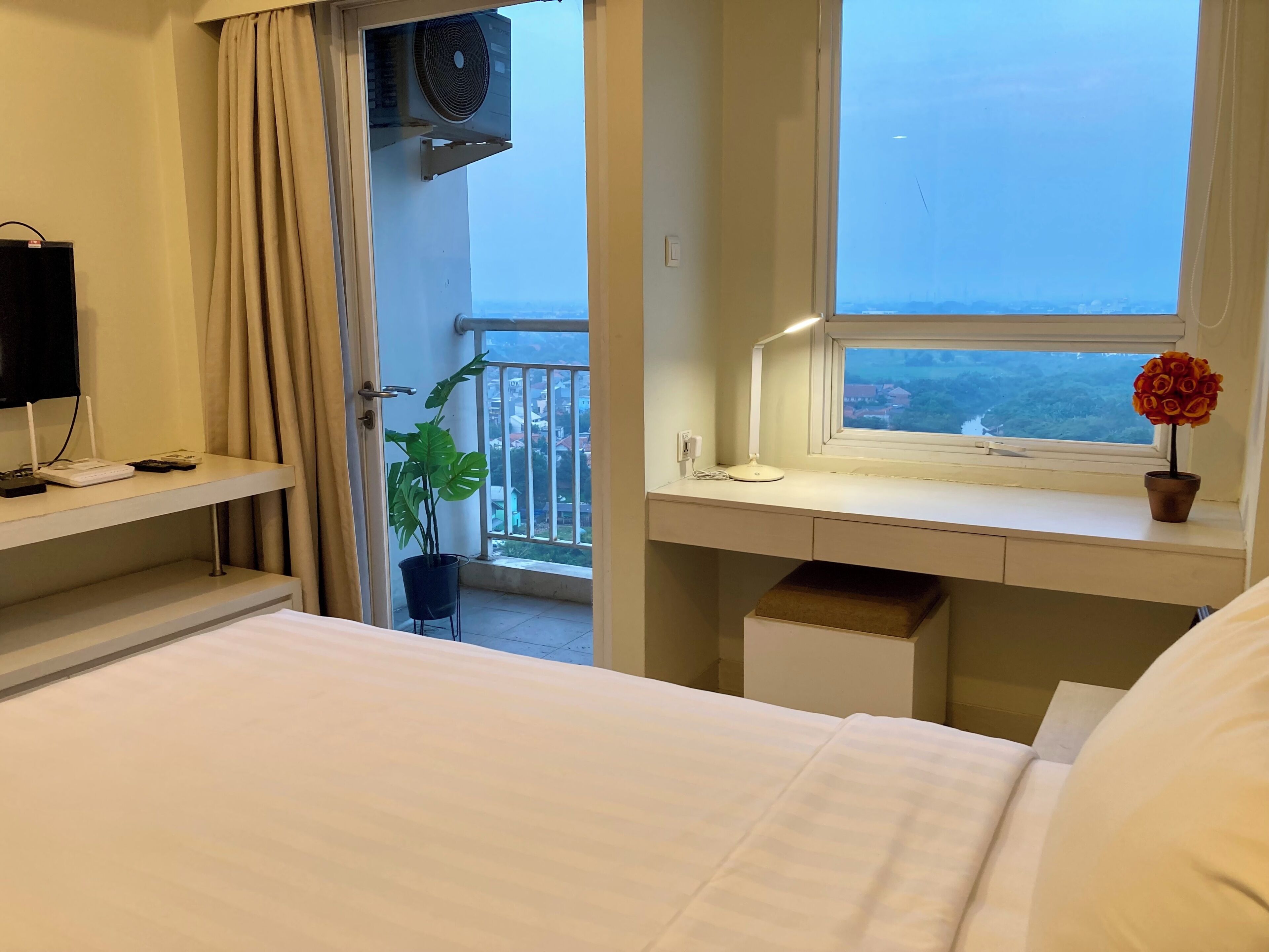 Une chambre d’hôtel avec un lit, un bureau équipé d’un ordinateur, une fenêtre donnant sur un paysage agréable et une plante en pot.