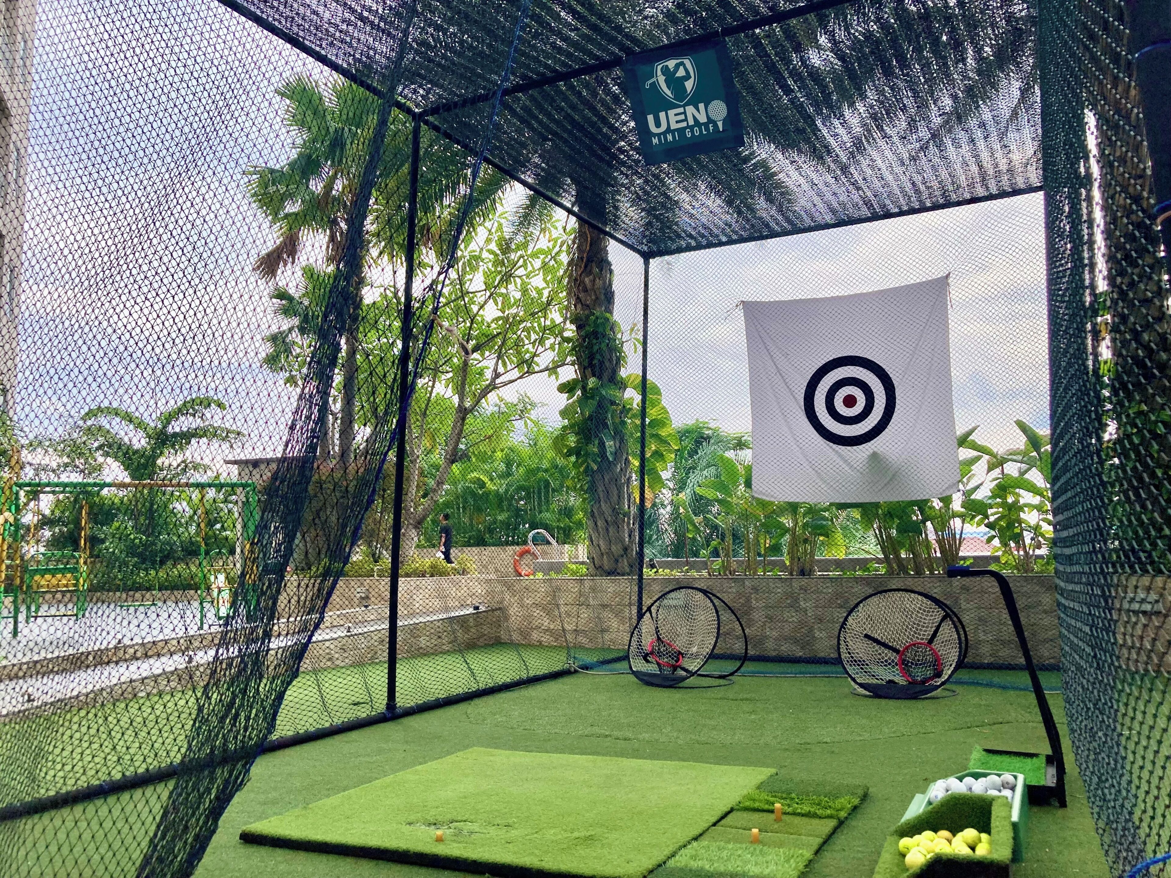 Un parcours de mini-golf doté d’un enclos grillagé, d’une cible et d’un panier de balles de golf.