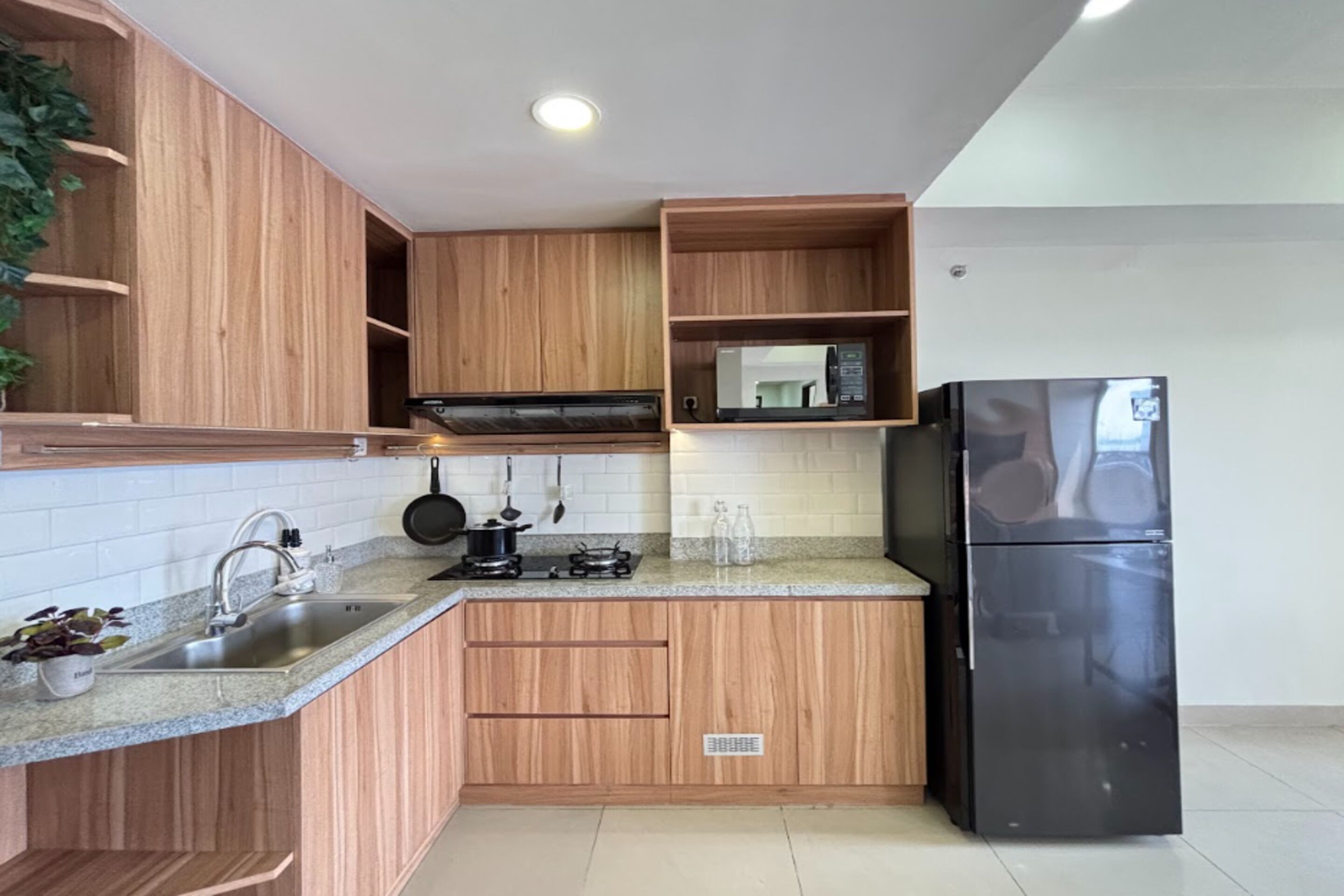 A kitchen with wooden cabinets, a stainless steel sink, a black refrigerator, and a microwave.