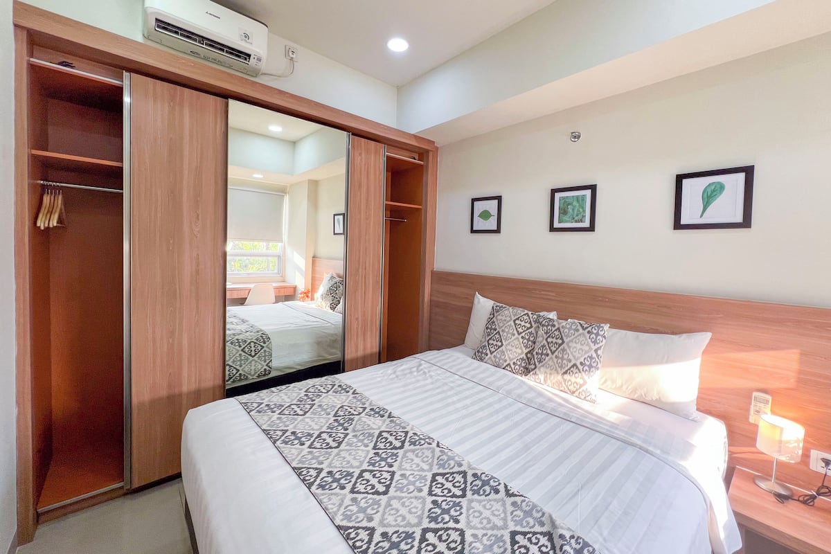 Un dormitorio con cama, armario, mesita de noche con lámpara y aire acondicionado instalado en la pared.