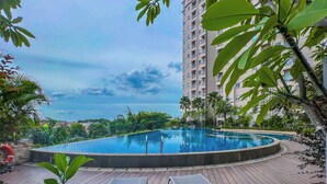 A swimming pool with lounge chairs, surrounded by greenery and a tall building in the background. - Merakey Golf Residence  (Cikarang)
