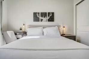 A hotel room with a large bed, a bedside table with a lamp, a chair, and a wall-mounted artwork of antlers. - 4 King/Queen Beds • 4 Private Baths • Near Garden of the Gods (Colorado Springs)
