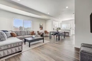 A modern living room with a sectional sofa, a coffee table, and a dining area with chairs and a table. - 4 King/Queen Beds • 4 Private Baths • Near Garden of the Gods (Colorado Springs)