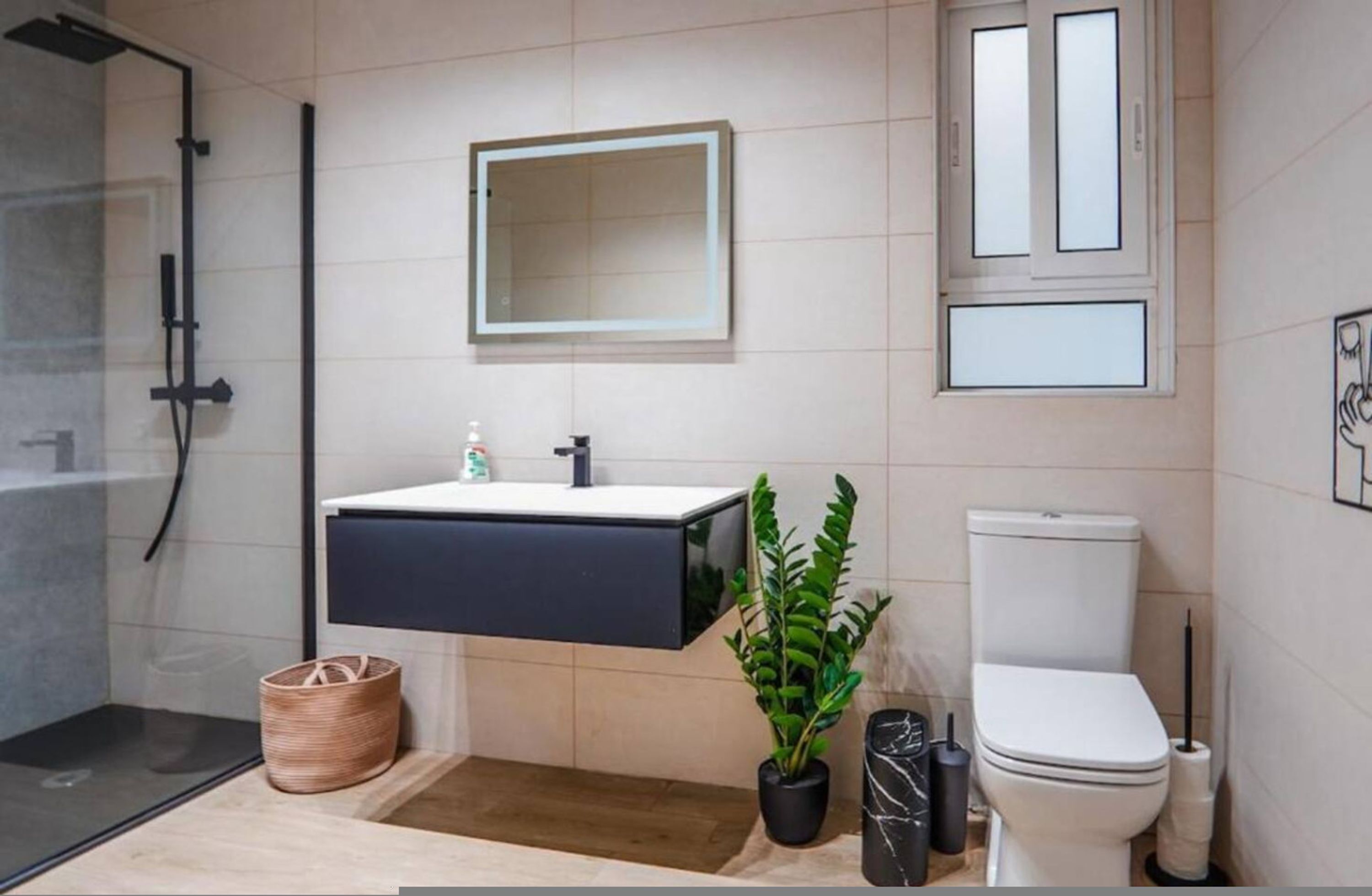 A modern bathroom with a glass shower enclosure, a black vanity, a toilet, and a potted plant.