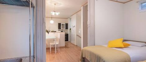 A bedroom with two beds, a desk, and a kitchenette.