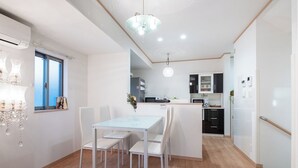 A modern kitchen with white cabinetry, a dining area with a glass table and white chairs, and a chandelier. - 4min to Station 3LDK Takadanobaba (Tokyo)