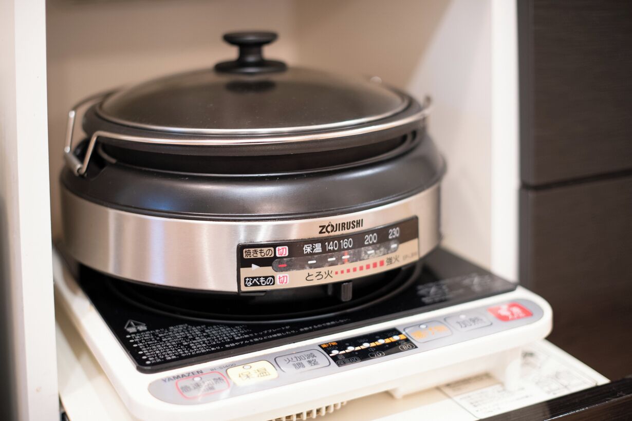A rice cooker with a digital display and control panel on a white countertop.