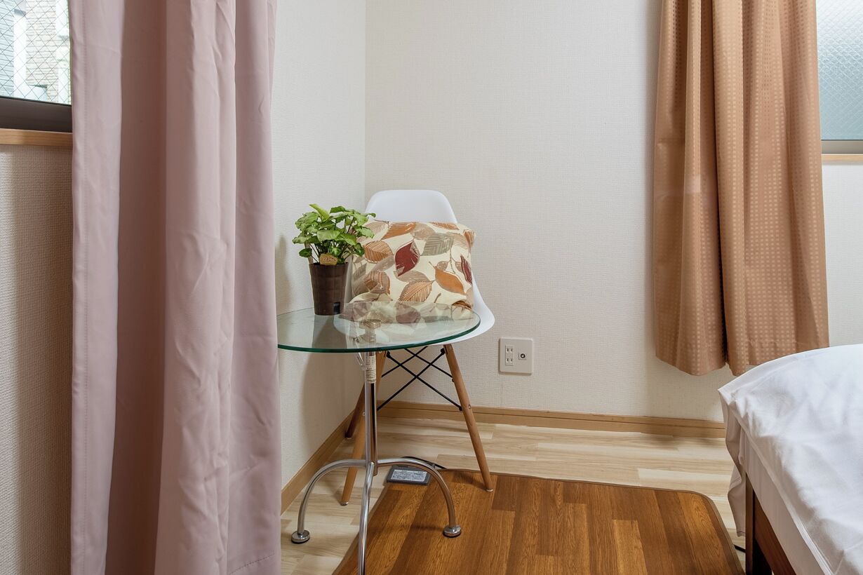 A small room with a bed, a glass table with a plant, and a chair with a patterned cushion.