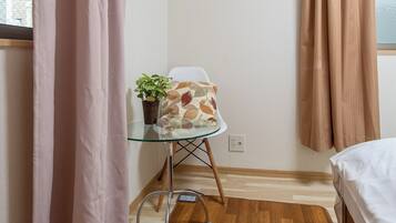 A small room with a bed, a glass table with a plant, and a chair with a patterned cushion.