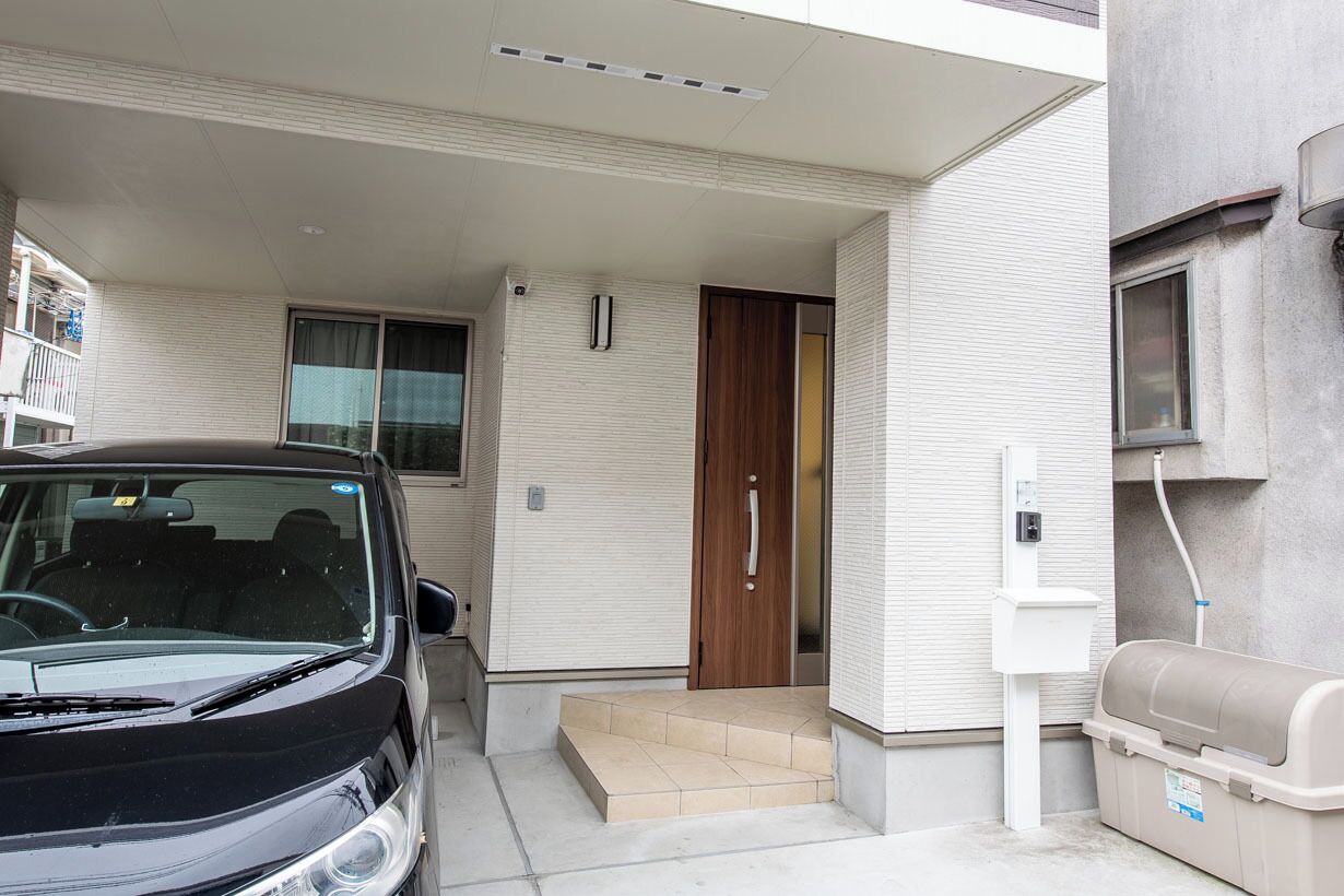 A car parked in front of a building with a door, a window, and a utility box.