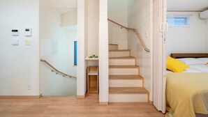 A room with a wooden staircase, a bed with a yellow pillow, and a small shelf with a green object. - 4min to Station 3LDK Takadanobaba (Tokyo)