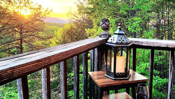 A wooden deck with a lantern, a table with a plate of food, and a glass of wine. - Sundance Retreat - Pet Friendly Mountaintop Cabin (Sevierville)