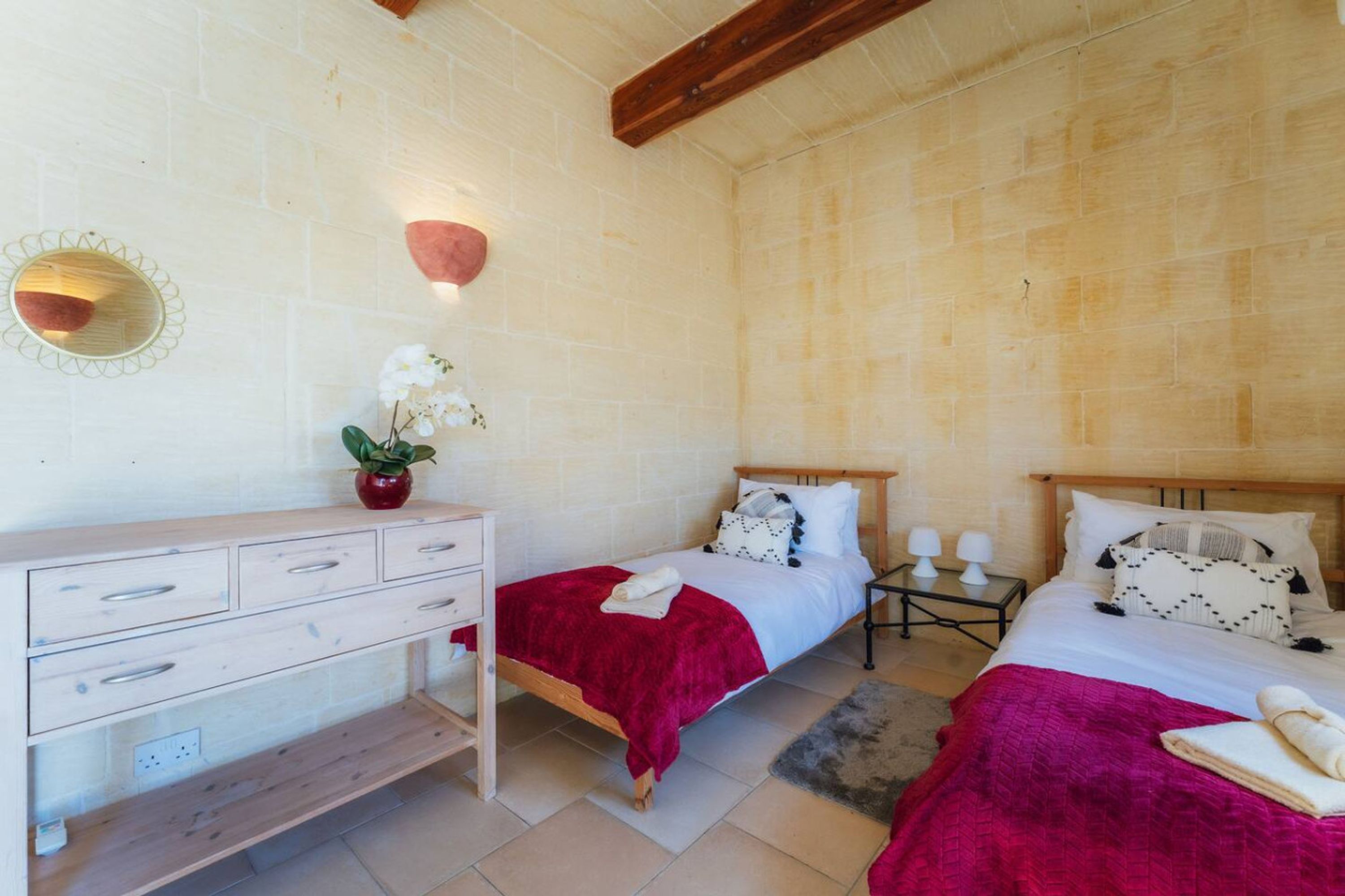 Un dormitorio con dos camas, un aparador de madera, un espejo, una mesita de noche con lámparas y una planta en maceta.
