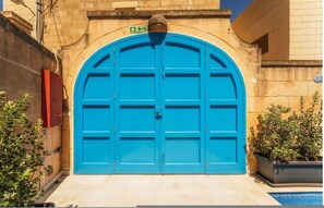 A blue arched door with a fire exit sign above it, set against a stone wall with a tiled floor and potted plants. - Authentic Xag ra Farmhouse With Private Pool (Xaghra)