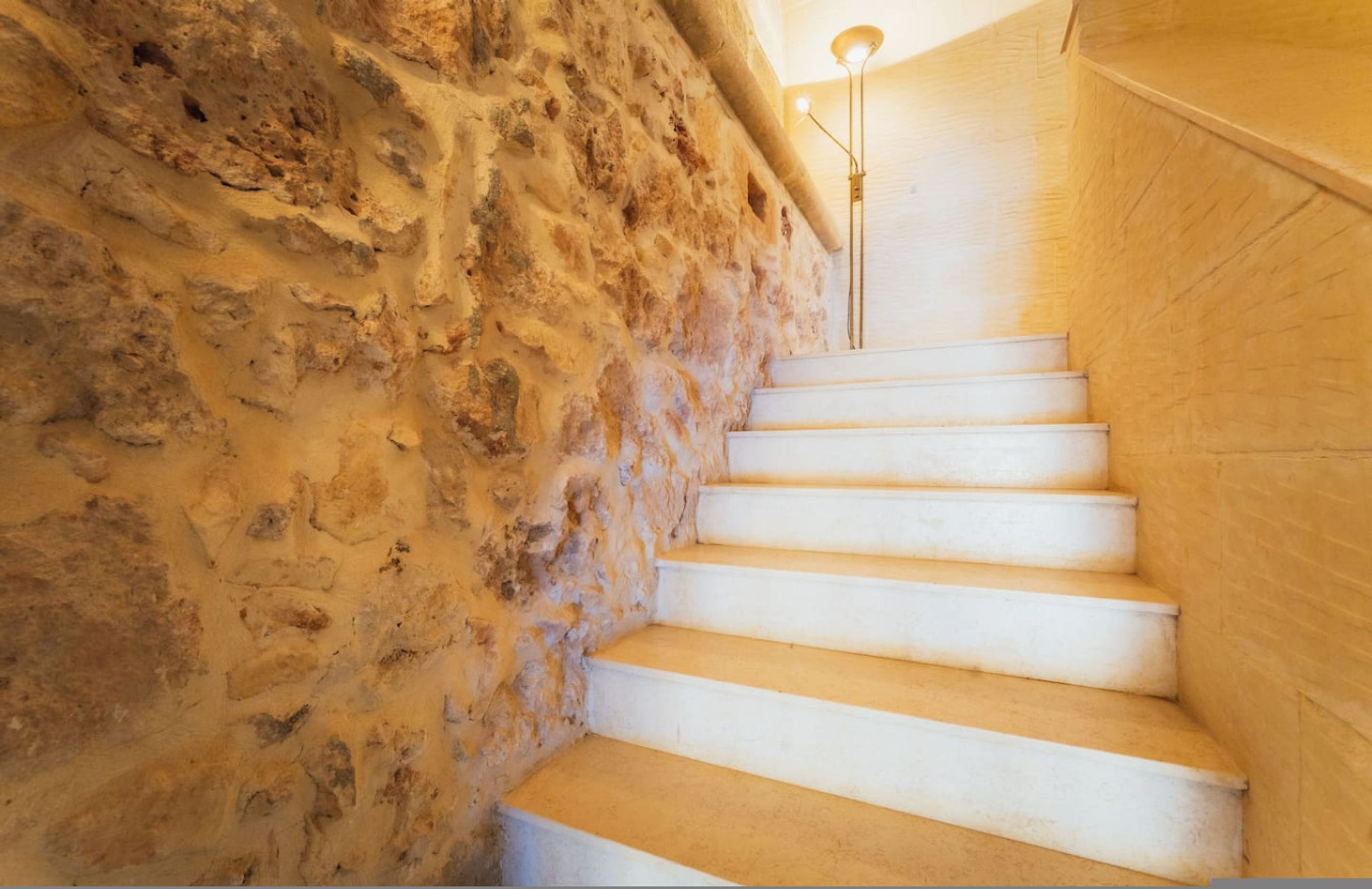 Una escalera de escalones blancos que sube hasta una plataforma, rodeada de paredes de piedra tosca.