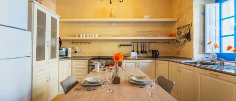 A kitchen with a wooden table set for dining, a chandelier, and a window with blue shutters.