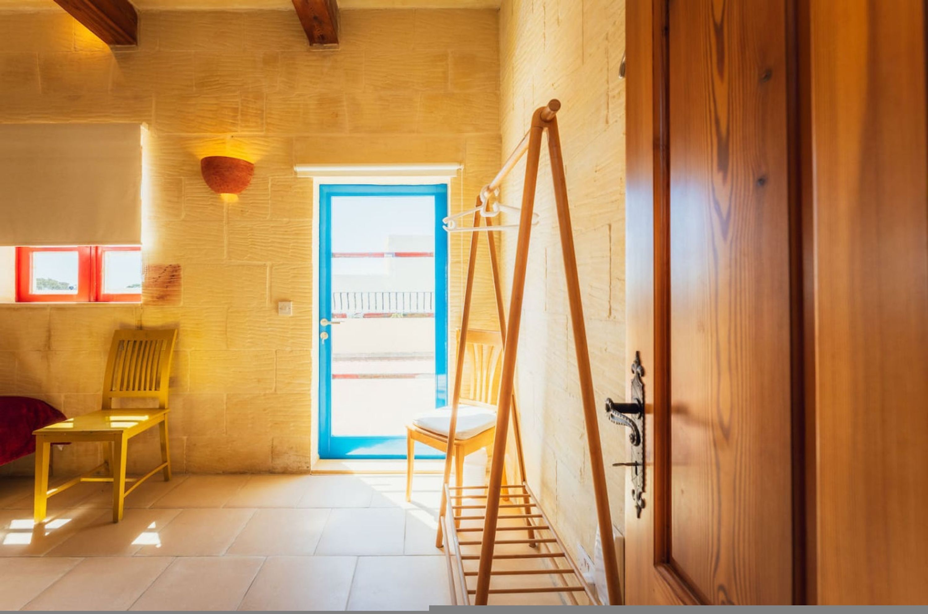 A room with a wooden door, a window with a view, a chair, and a wall-mounted rack.