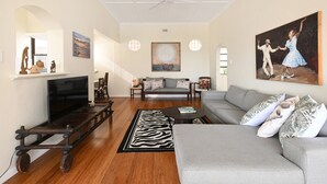 A living room with a sofa, a television, a wooden coffee table, a zebra-patterned rug, and a painting on the wall. - Sea View Ocean Facing Spacious 1 Bedroom Apartment (Cape Town)