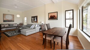 A spacious living room with a sofa, a dining table, and chairs, a ceiling fan, and artwork on the walls. - Sea View Ocean Facing Spacious 1 Bedroom Apartment (Cape Town)