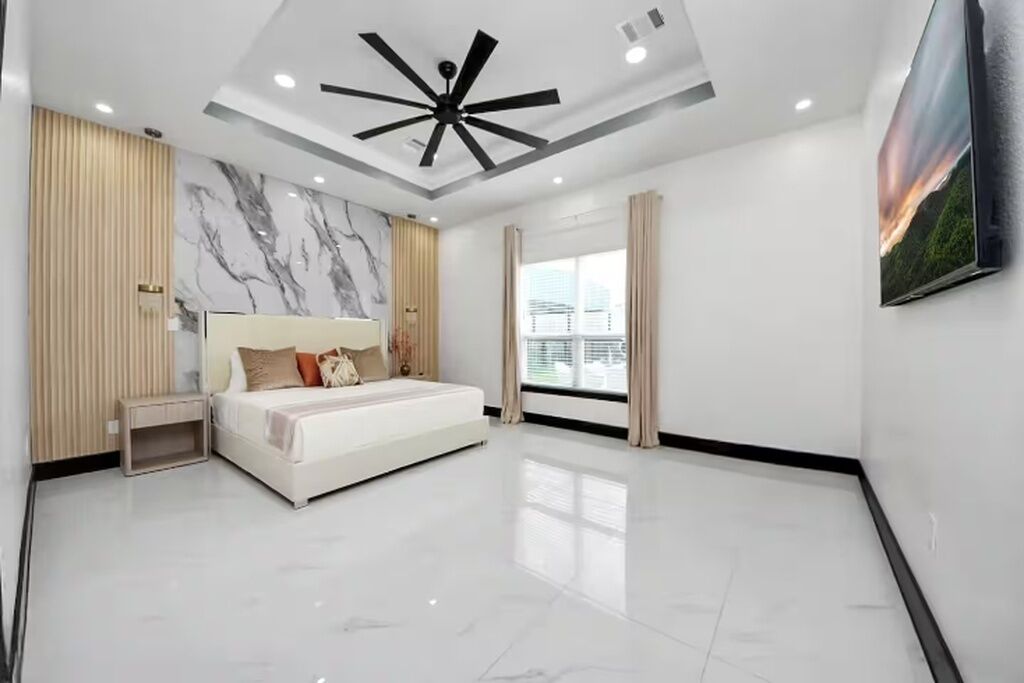 A modern bedroom with a bed, a ceiling fan, and a large window.
