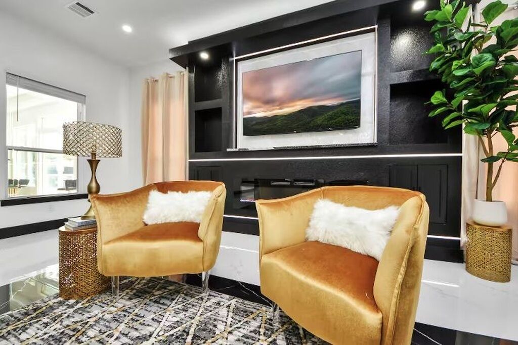 Een moderne woonkamer met een grote televisie, twee comfortabele fauteuils, een vloerkleed met patroon en een plant.