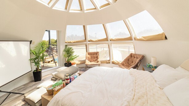 A bedroom with a skylight, large windows, a bed, a chair, a bedside table, and a potted plant. - Sleeps 30, Private Ranch, 15 acre, Pool, Pond, sauna, pikleball court near DFW (Corsicana)