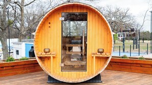 A wooden barrel-shaped structure with a glass door, a small shelf with items, and a basketball hoop in the background. - Sleeps 30, Private Ranch, 15 acre, Pool, Pond, sauna, pikleball court near DFW (Corsicana)