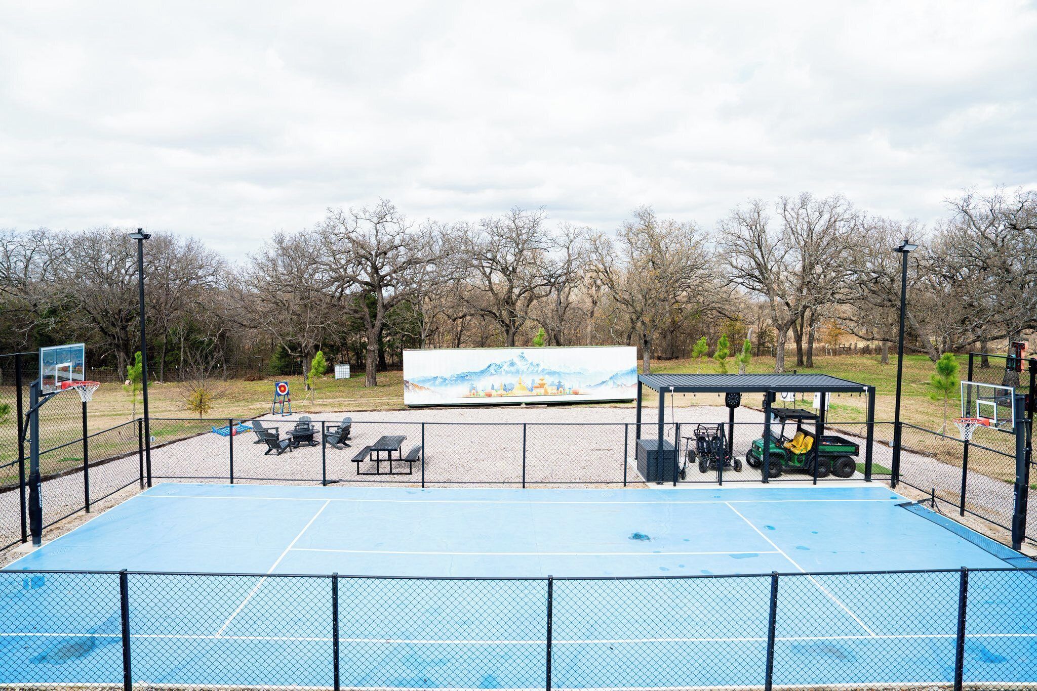 An outdoor basketball court with a fence, a bench, and a golf cart.