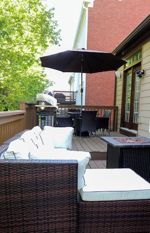 Une terrasse extérieure avec des meubles en osier, un barbecue et un parasol.
