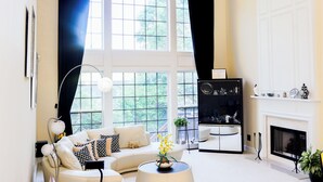 Ein Wohnzimmer mit einer Couch, einem Couchtisch, einem Kamin und einem großen Fenster mit Vorhängen.