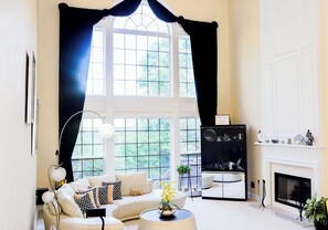 Ein Wohnzimmer mit einer Couch, einem Couchtisch, einem Kamin und einem großen Fenster mit Vorhängen.