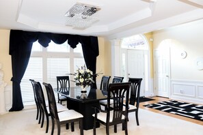 Une salle à manger avec une table noire, des chaises blanches, un vase de fleurs et des rideaux noirs.