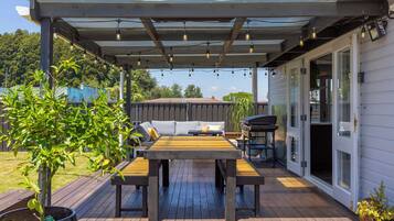 En overdækket terrasse med et træbord og stole, grill og en pergola med lyskæder.