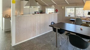 Et moderne køkken med en central ø, et spiseområde med bord og stole, samt et vindue der giver udsigt til det fri.