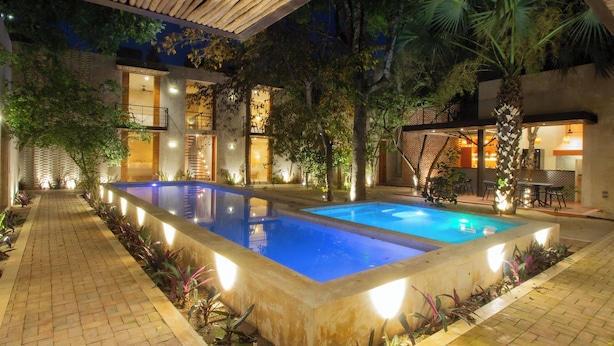 A pool area with a tiled deck, surrounded by plants and trees, and a building with balconies and lights. - Hotel Boutique Alma Peregrina (Valladolid)