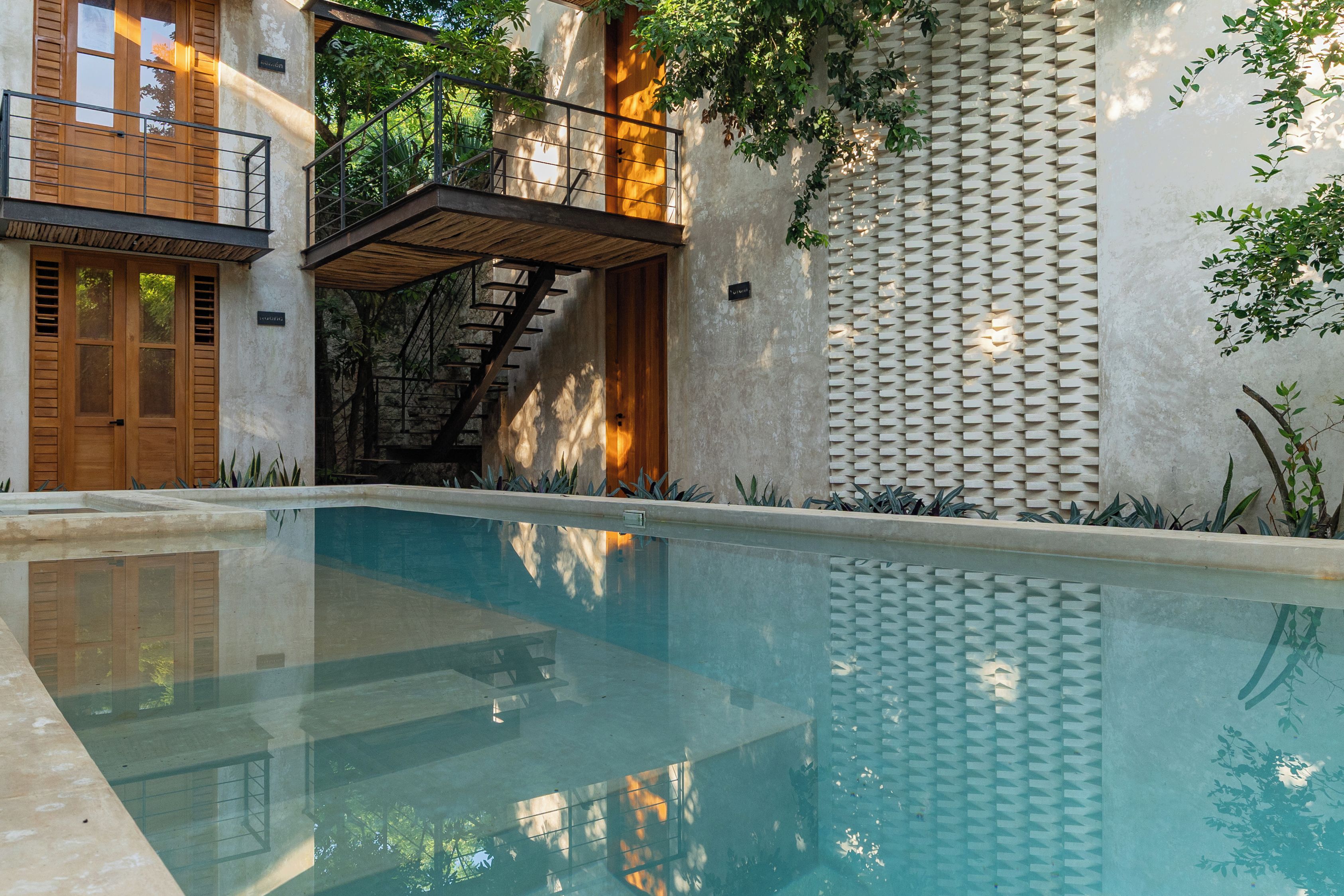 A swimming pool with a wooden deck, a staircase, and a wall with a textured pattern.